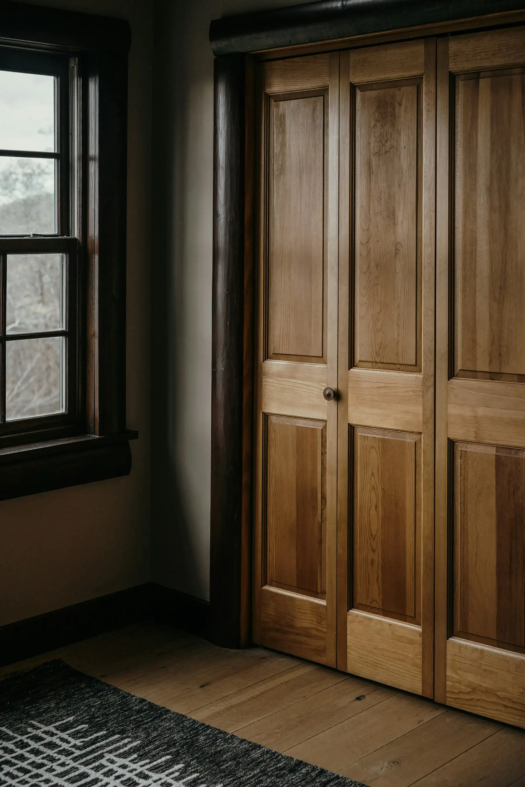 Armoire encastrée à portes à cadre et panneaux en bois massif, près d’une fenêtre