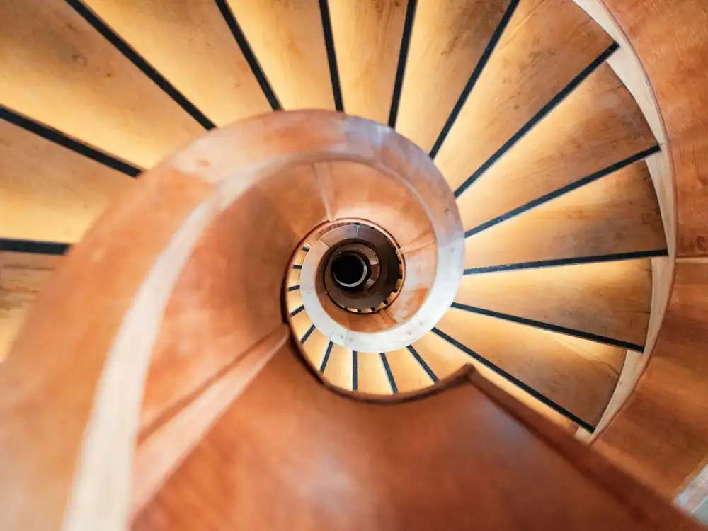 Escalier en colimaçon en bois vu en plongée, main courante cintrée et marches rayonnantes