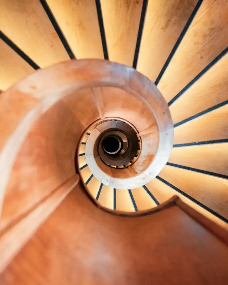 Escalier en colimaçon en bois vu en plongée, main courante cintrée et marches rayonnantes