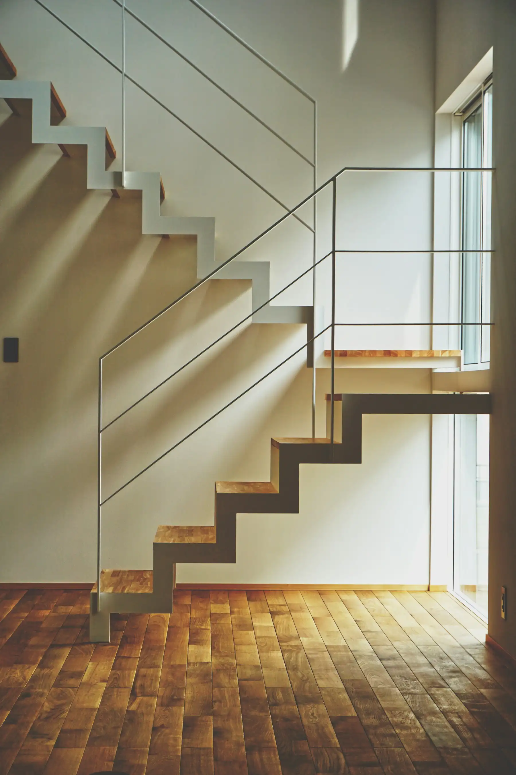 Treppe mit Holzstufen und weisser Metallwange im Sonnenlicht über einem Parkettboden