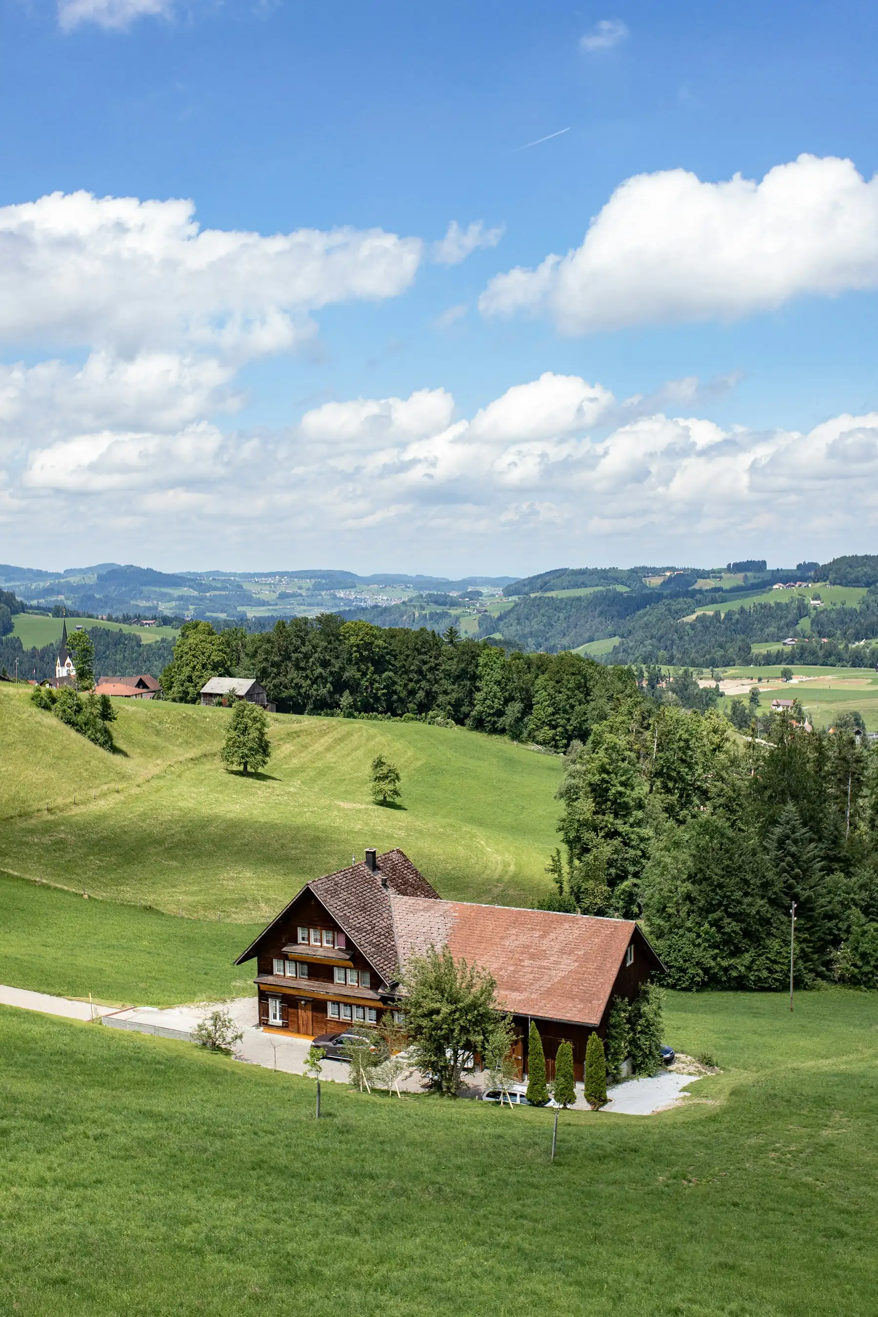 Ferme traditionnelle à grand toit dans les collines verdoyantes des Préalpes