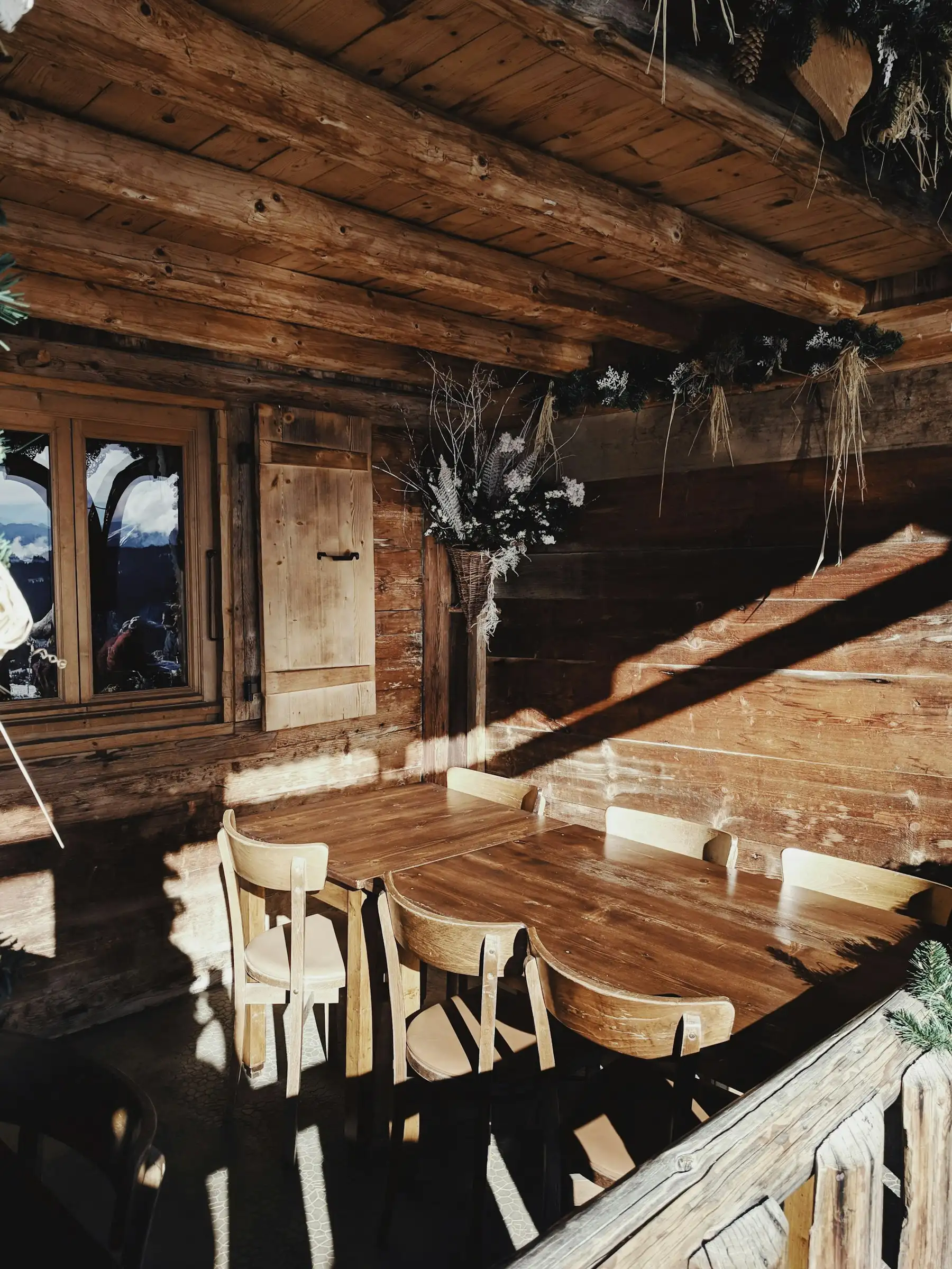 Intérieur de chalet ancien en madriers, table et chaises en bois dans un rayon de soleil