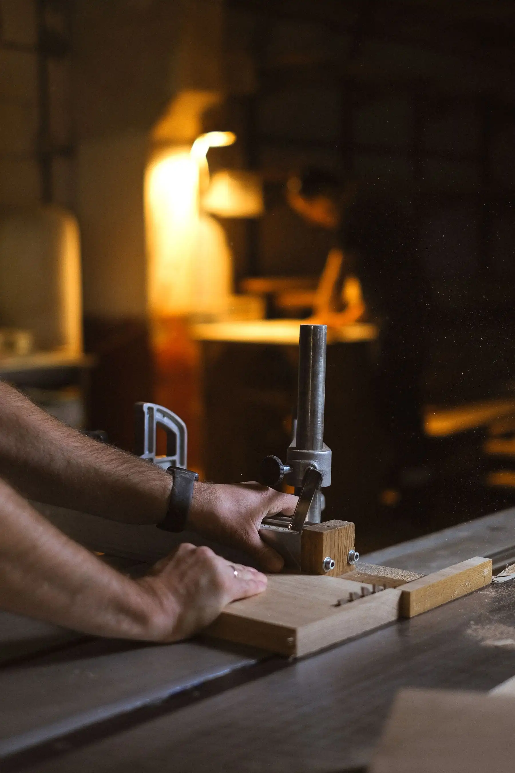 Avant-bras d’artisan guidant une pièce sur une machine stationnaire, lampe d’atelier chaude en arrière-plan